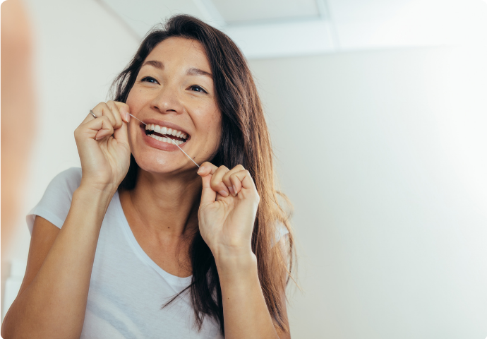 Asian woman flossing teeth in front of mirror to maintain healthy gums and oral hygiene